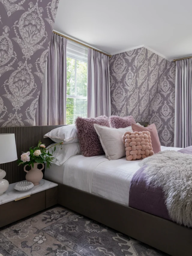 Designing around architectural challenges often yields the most beautiful results. 💜

In the primary bedroom at #ProjectDutchColonialDelight, we embraced the angles of the space rather than fighting them. Our clients requested a king bed with nightstands on each side. However, the wall that the previous owners had placed the bed on didn’t have enough room to accommodate this. (Swipe left to see the before pics.) The solution? A reeded platform bed with integrated nightstands that nestles perfectly into the eaves, transforming what could have been an awkward area into a focal point.

While the bed grounds the space, the wallpaper is truly the star of the show. Its dramatic pattern sets the tone for the entire room. Layered throughout the space, shades of our client’s favorite color, purple, infuse warmth, personality, and depth. Striped linen motorized draperies add softness and texture while introducing another layer of pattern, proving that thoughtfully paired elements can create a balance that feels both bold and harmonious.

The redesign wasn’t just about fitting a king bed. By reworking the furniture plan, we improved the room’s circulation, creating a seamless path to the walk-in closet and primary bath without having to navigate around the bed.

One of our favorite original details? The curved wall corner. (Swipe left!) We echoed that gentle curve in the platform bed, dresser, and occasional chair, softening the strong lines and angles of the architecture. These details create harmony throughout the room and result in a primary bedroom that feels cozy, intentional, and completely unique to the homeowner.

#SWANKByDesign #PrimaryBedroom #Purple #InteriorDesign
